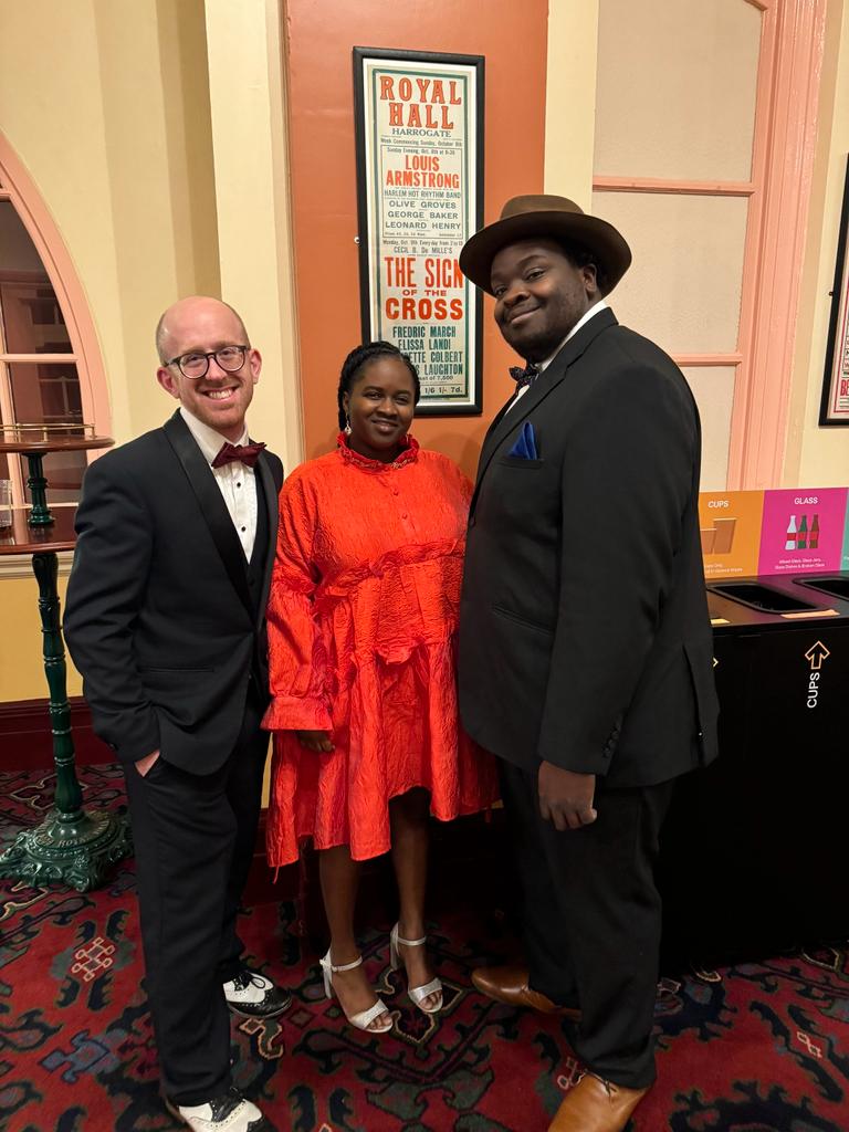 Mike Paul-Smith, Marvin Muoneké and Ineza in front of the Louis Armstrong poster at The Royal Hall, Harrogate